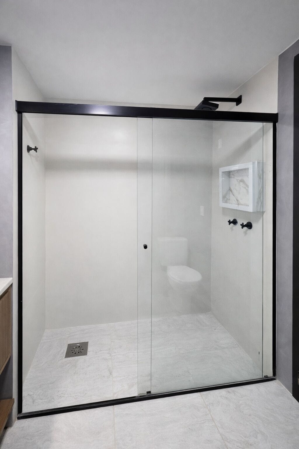 Un bagno moderno con doccia vetrata, un water e un piccolo ripiano con articoli da toilette.