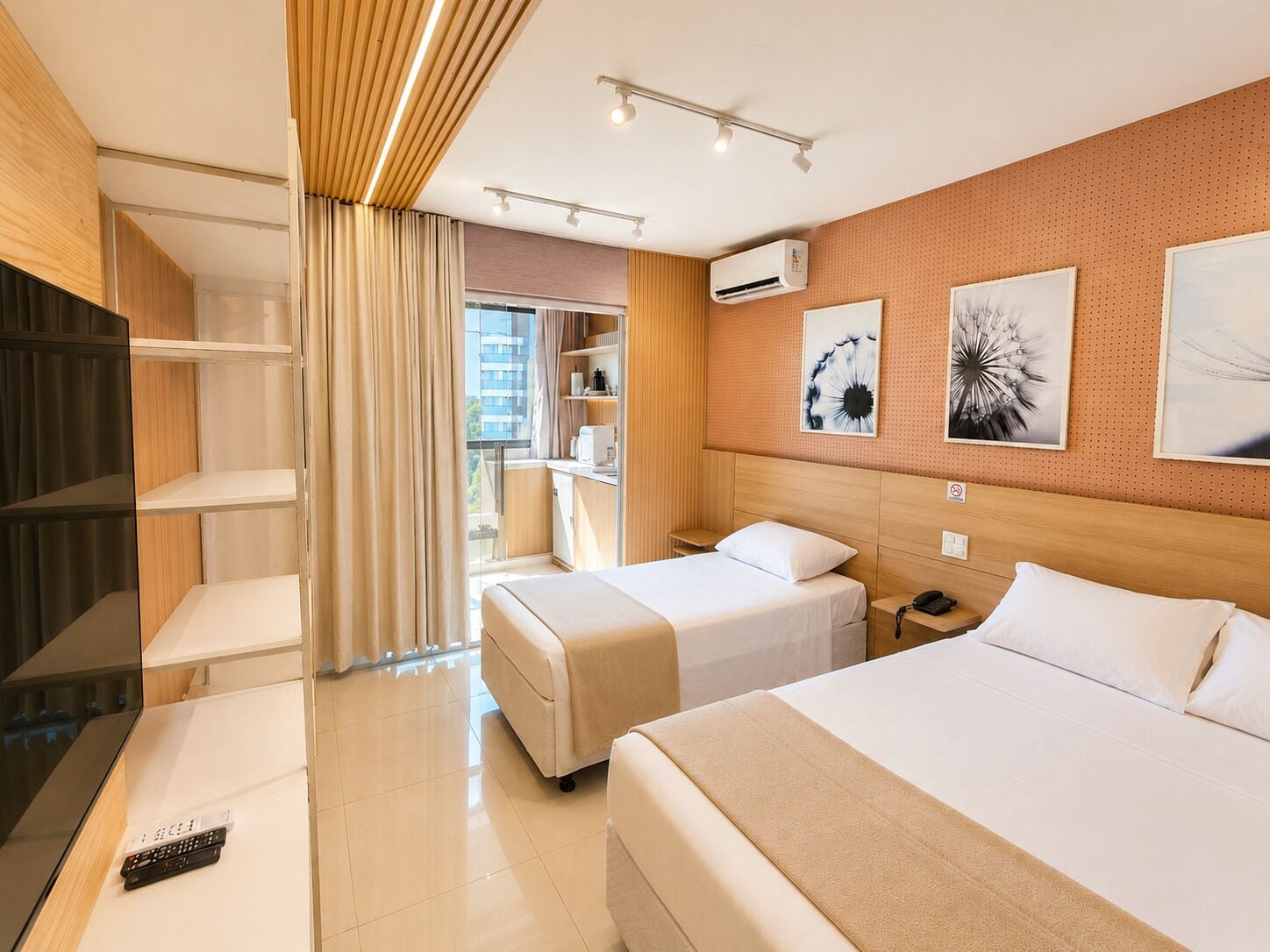 A hotel room with two beds, a TV, a desk, and a window with curtains.