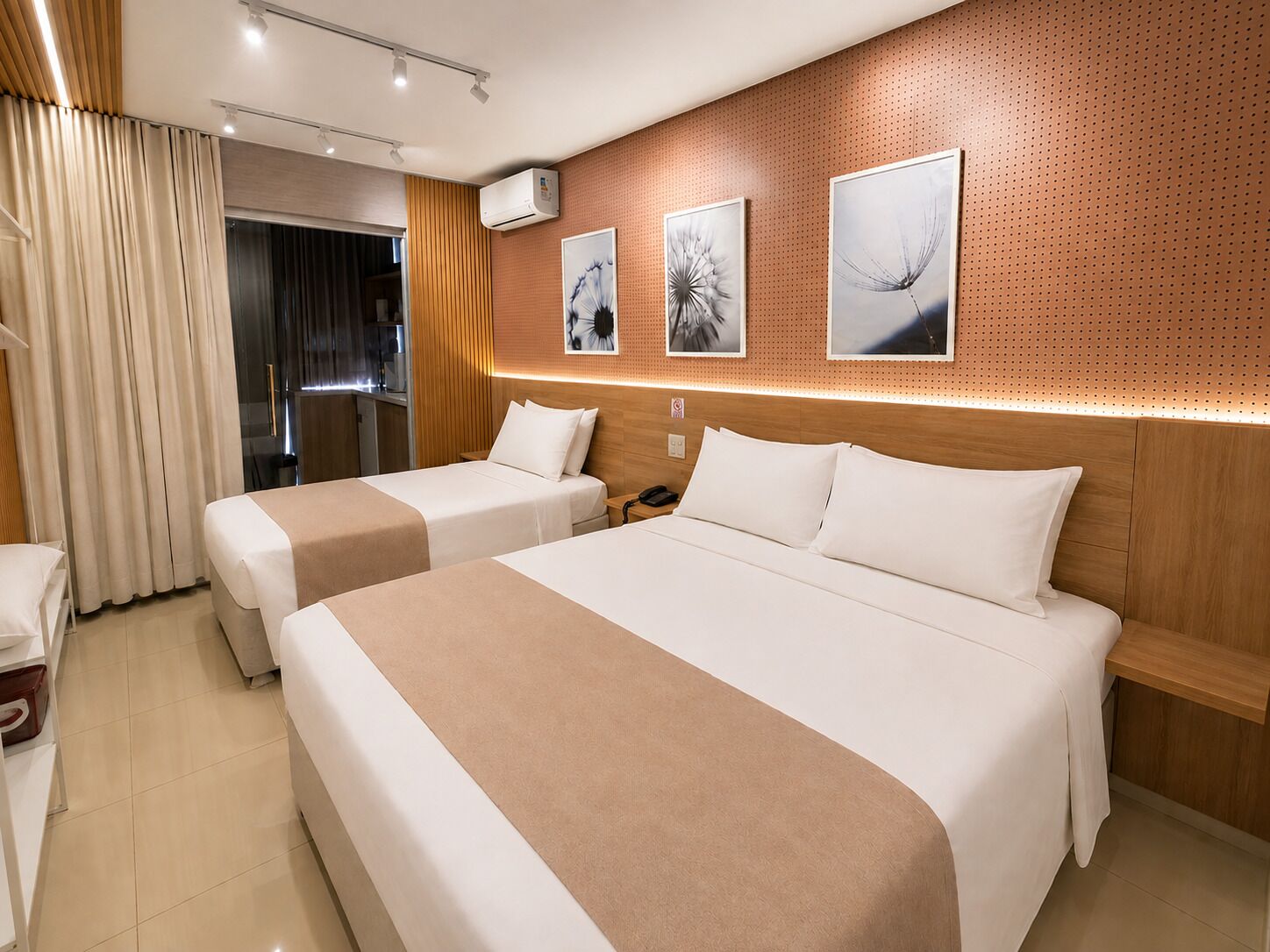 Een hotelkamer met twee bedden, een houten hoofdbord, een wandairconditioner en kunstwerk.