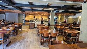 A restaurant with wooden tables and chairs, a central counter with a chef, and a brick wall.