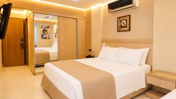 A hotel room with a large bed, a bedside table, an air conditioning unit, a wardrobe, and a television.