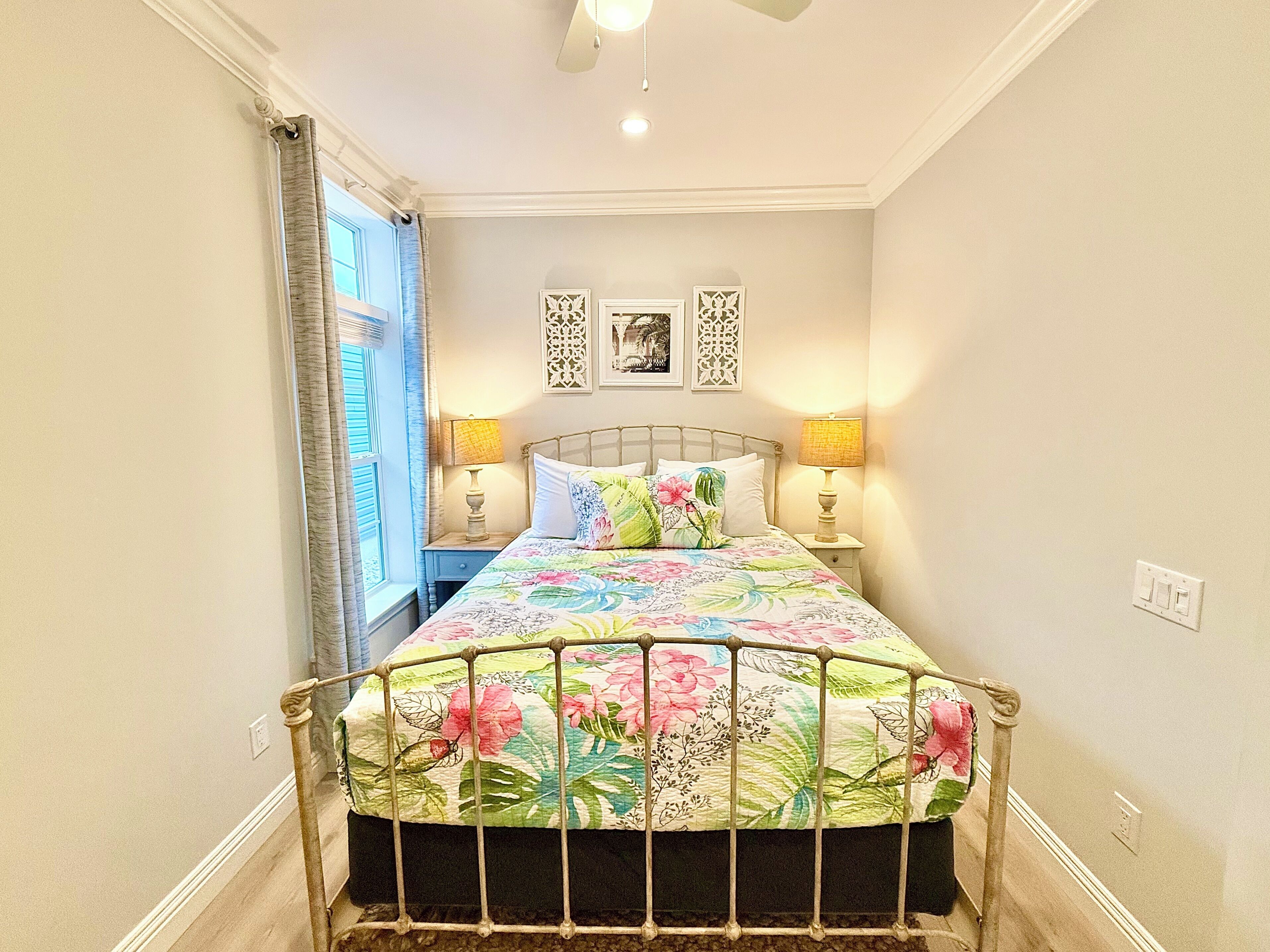 A bedroom with a bed, two bedside lamps, a window with curtains, and decorative wall art.