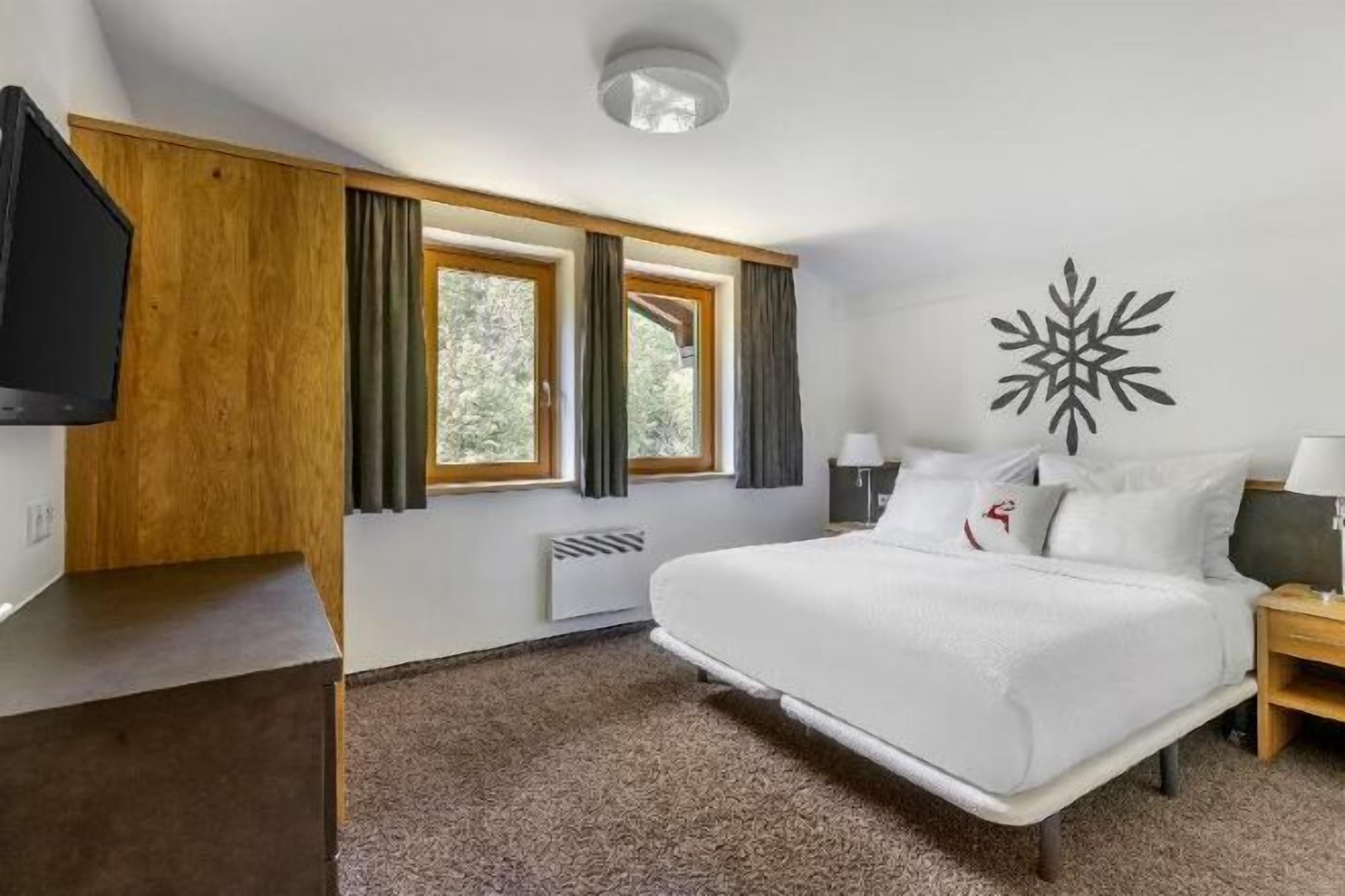 Una habitación de hotel con una cama, televisión, ventana con cortinas, un adorno en la pared y una mesita de noche.