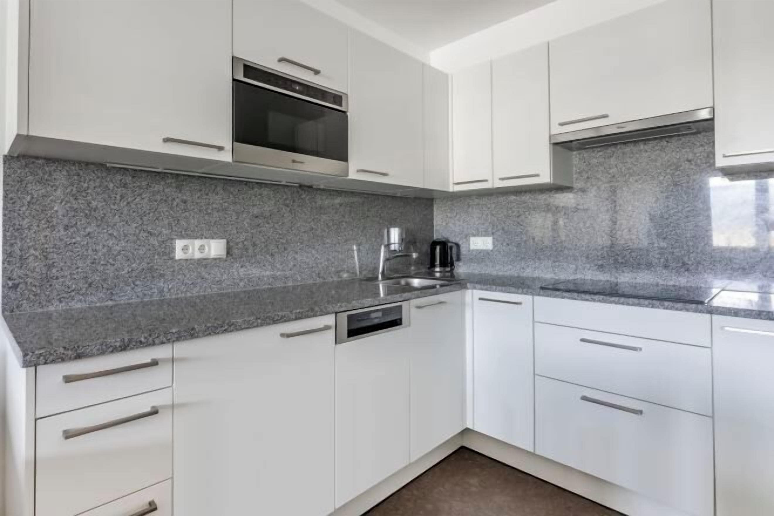 A modern kitchen with white cabinets, a granite countertop, a built-in oven, and a coffee maker.