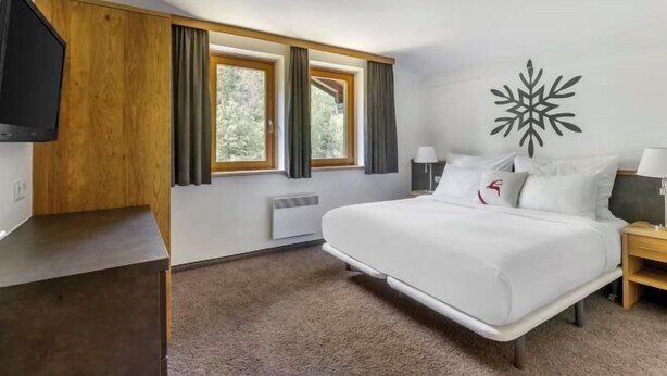 A modern hotel room with a bed, a TV, a large window, and a decorative wall piece. - Alpine Club Resort (Schladming)