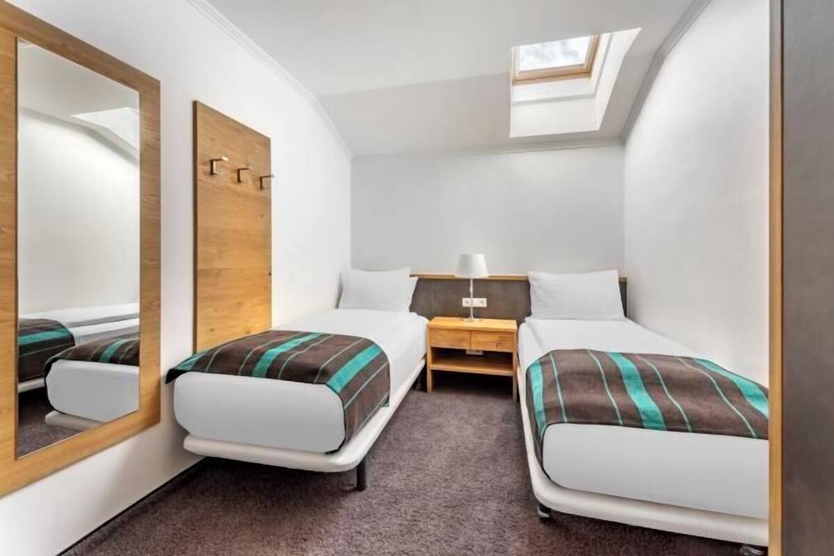 A small, modern room with two beds, a mirror, a nightstand, and a skylight.