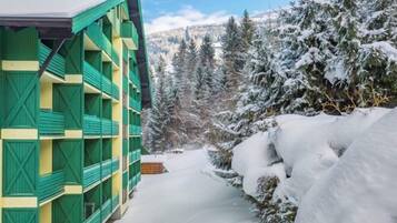 Un edificio de varios pisos con paredes exteriores verdes y amarillas, rodeado de árboles cubiertos de nieve y un cielo despejado.