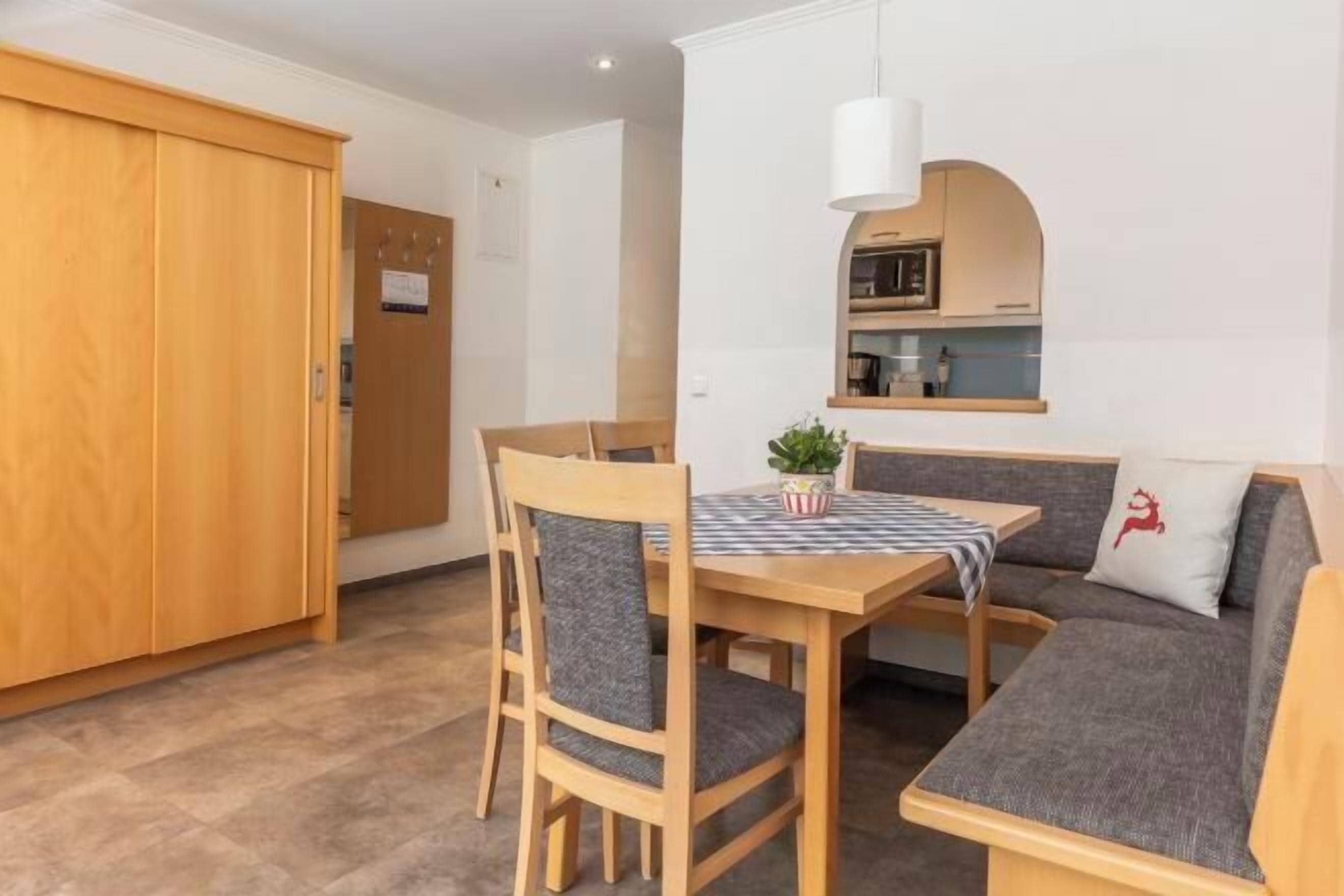 A dining area with a wooden table, chairs, a bench, and a small kitchen area with a microwave.