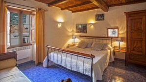 Une chambre avec un plafond en bois, un lit avec un cadre en métal, deux lampes de chevet, un radiateur et une fenêtre avec des rideaux.