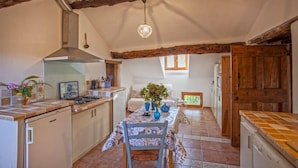 Une cuisine équipée d’une cuisinière à gaz, d’un évier et d’un plafond en bois. On y trouve une table à manger avec des chaises et un vase de fleurs.