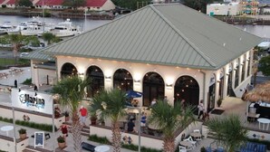 A waterfront building with a covered patio area, featuring outdoor seating and potted plants.
