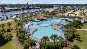 A large, uniquely shaped swimming pool with multiple sections and lounge areas, surrounded by palm trees and a marina with boats.