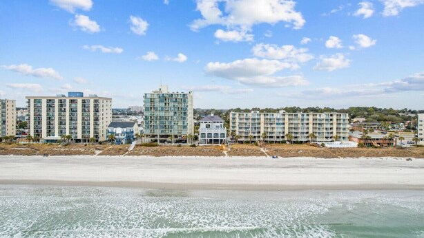 A beachfront hotel with multiple buildings, including a prominent glass tower, and a sandy beach in the foreground.