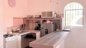 A compact kitchen with a gas stove, microwave, and refrigerator, a small sink, and a window with bars. - HOUSE IN LO DE MARCOS, NAYARIT - UP TO 8 PEOPLE AND PETS (Lo de Marcos)
