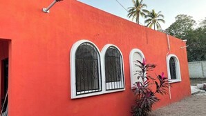 A building with a bright orange exterior, three arched windows with black metal bars, and a small plant in the foreground. - HOUSE IN LO DE MARCOS, NAYARIT - UP TO 8 PEOPLE AND PETS (Lo de Marcos)