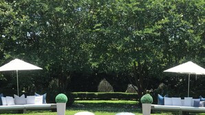 A pool area with a rectangular pool, surrounded by a well-maintained lawn and trees. There are two white umbrellas providing shade. - IF Stay Collection is an exquisite and unexpected stand alone Row House. (Carriere)