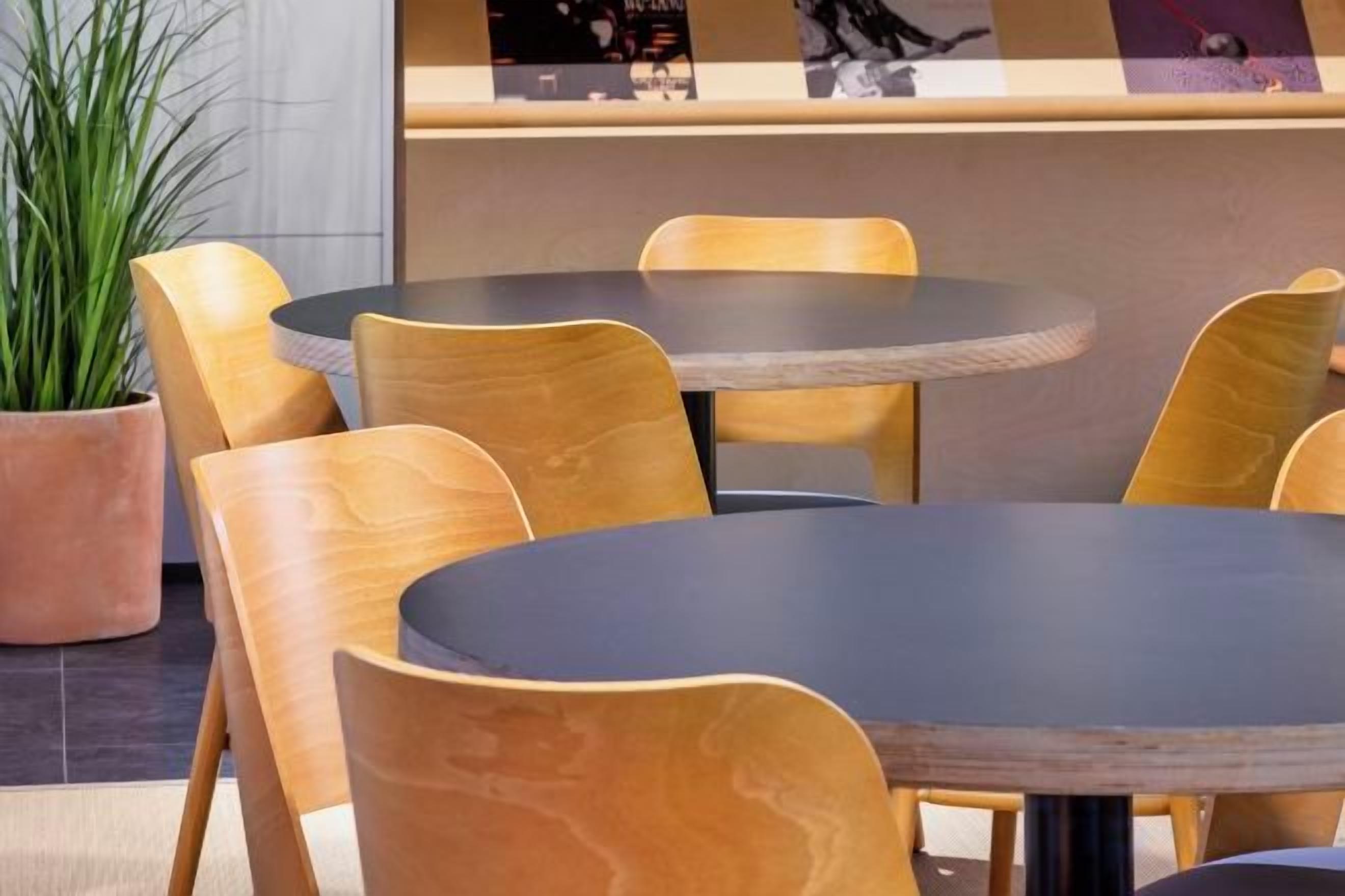 A seating area with round tables and wooden chairs, a potted plant, and a counter with a menu.