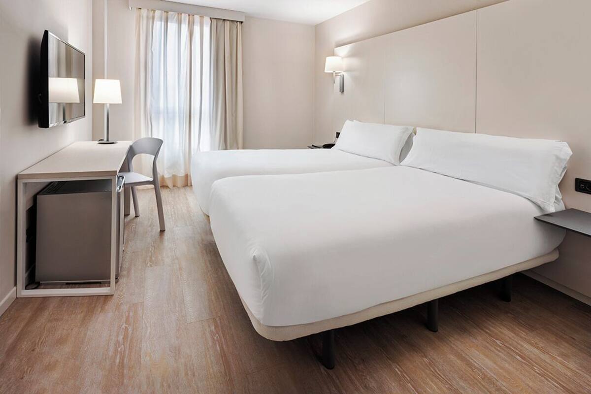 Habitación de hotel con dos camas, un escritorio, una silla, un televisor y una ventana con cortinas.