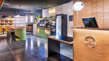 A modern hotel lobby with a reception desk, seating area, and a bar.