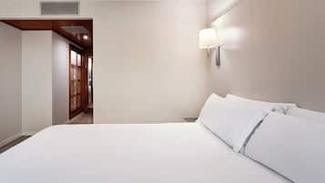 Een hotelkamer met een groot bed, een wandlamp en een houten deur naar een gang.