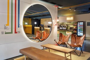 Un interior moderno con un espejo circular, zona de estar y una barra con letrero de neón.