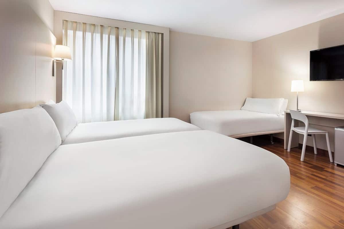 Habitación de hotel con dos camas, un escritorio, una silla, un televisor y una ventana con cortinas.