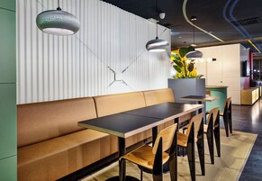 Un interior moderno con una larga mesa de madera, asientos acolchados, iluminación colgante y una planta en maceta.
