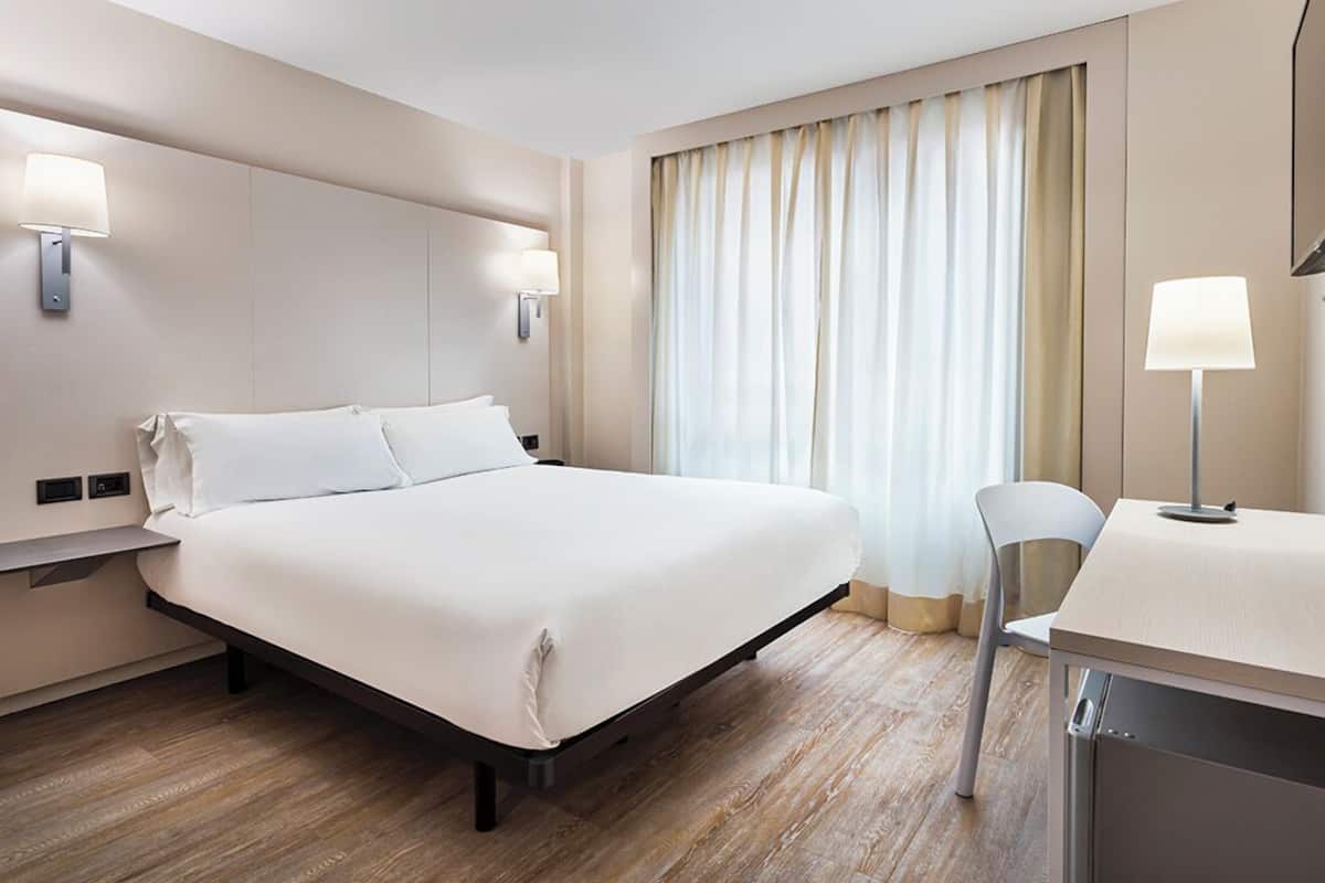 Una habitación de hotel con cama, lámparas de noche, escritorio y una silla.