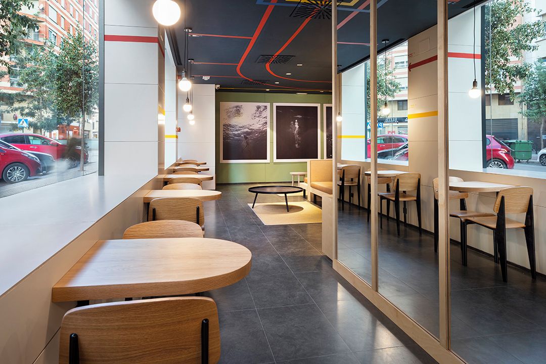 A modern cafe with wooden tables and chairs, large windows, and artwork on the walls.