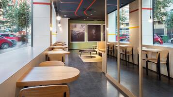 A modern cafe with wooden tables and chairs, large windows, and artwork on the walls.