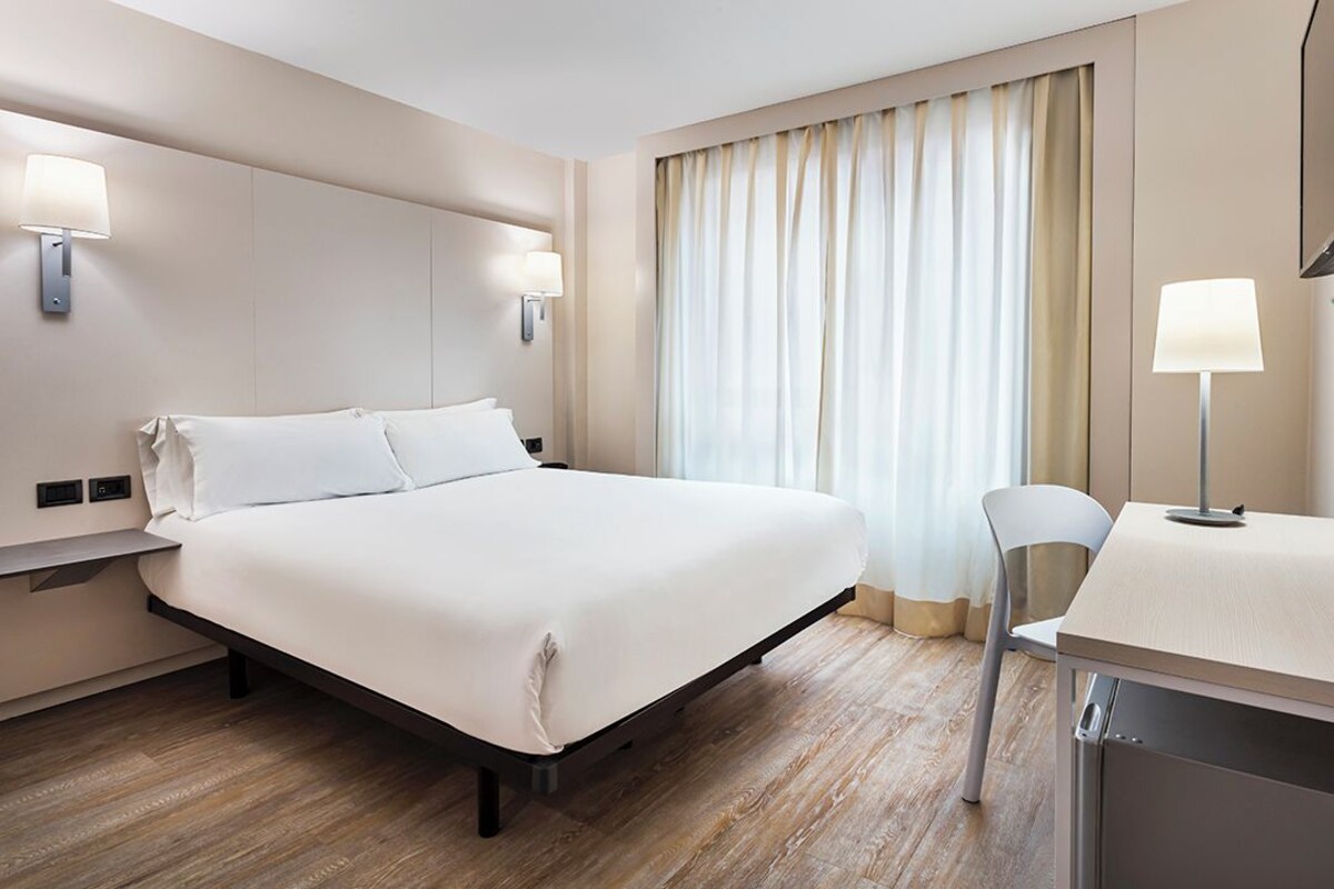 Una habitación de hotel con cama, lámparas de noche, escritorio y una silla.
