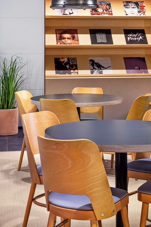 Un comedor con mesas redondas y sillas de madera, una planta en maceta y una pared con carteles enmarcados.