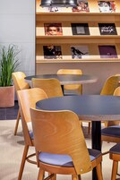 Un comedor con mesas redondas y sillas de madera, una planta en maceta y una pared con carteles enmarcados.