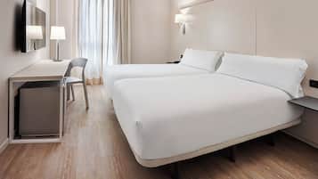 A hotel room with two beds, a desk, a chair, a TV, and a window with curtains.