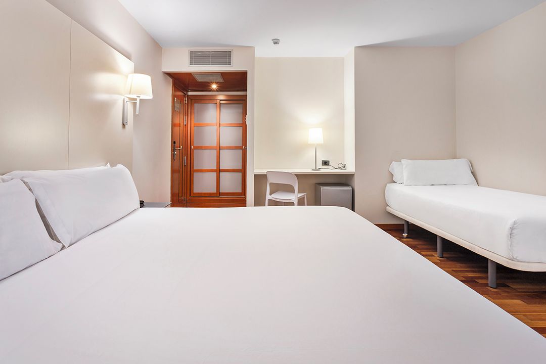 A hotel room with a large bed, a desk, a chair, and a wardrobe.