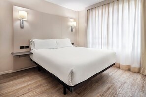 A hotel room with a large bed, two wall-mounted lamps, a nightstand, and a window with curtains. - B&B Hotel Castellón (Castelló de la Plana)