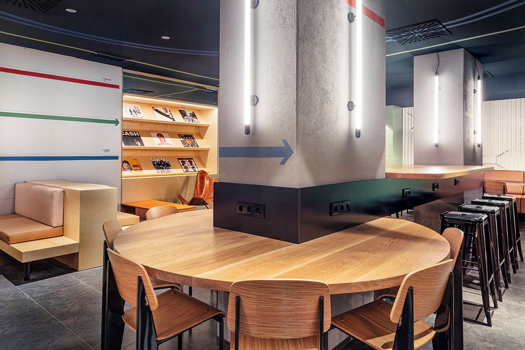 A modern interior with a wooden table and chairs, a sofa, and a bar area with stools.