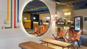 A modern interior with a circular mirror, seating area, and a counter with a neon sign. - B&B Hotel Castellón (Castelló de la Plana)