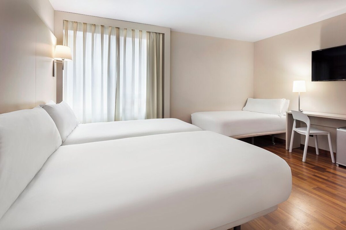 Habitación de hotel con dos camas, un escritorio, una silla, un televisor y una ventana con cortinas.