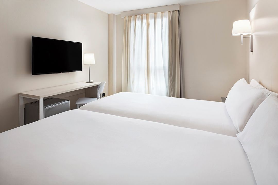A hotel room with two beds, a flat-screen TV, a desk, and a lamp.