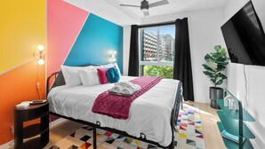 A modern hotel room with a bed, a ceiling fan, a TV, a potted plant, and a view of buildings outside. - King Bed, Gym, 2min walk to UAB, Foodie Haven (Birmingham)