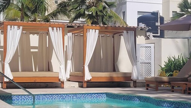 A poolside area with two wooden cabanas with white curtains, a pool with blue mosaic tiles, and lounge chairs. - Villa Mare B5 (on the Beach) Bavaro Los Corales (Punta Cana)