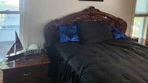 Une chambre à coucher avec une tête de lit en bois, un lit recouvert d’une literie sombre, une table de chevet avec une lampe et un tableau encadré au mur.