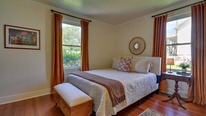 Ein Schlafzimmer mit einem Bett, einer Bank, einem Nachttisch, einem Fenster und einem Bild an der Wand.