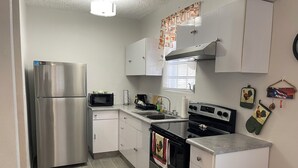 Una cocina compacta con refrigerador de acero inoxidable, microondas, estufa y pileta.