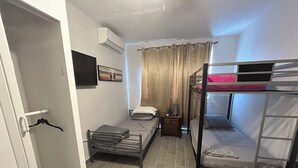 Habitación compacta con literas, una mesita de noche pequeña, aire acondicionado de pared y una puerta con perchero.