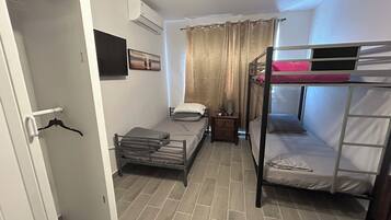 A compact room with bunk beds, a small bedside table, a wall-mounted air conditioner, and a door with a coat rack.