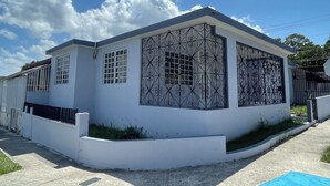 Un edificio moderno blanco con un gran ventanal con intrincados detalles metálicos, un acceso con reja y un cielo azul despejado al fondo.