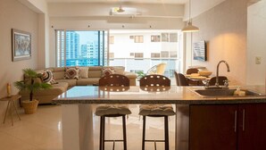 A modern kitchen with a central island, pendant lighting, and a view of a high-rise building. - Poseidon del Caribe (Cartagena)