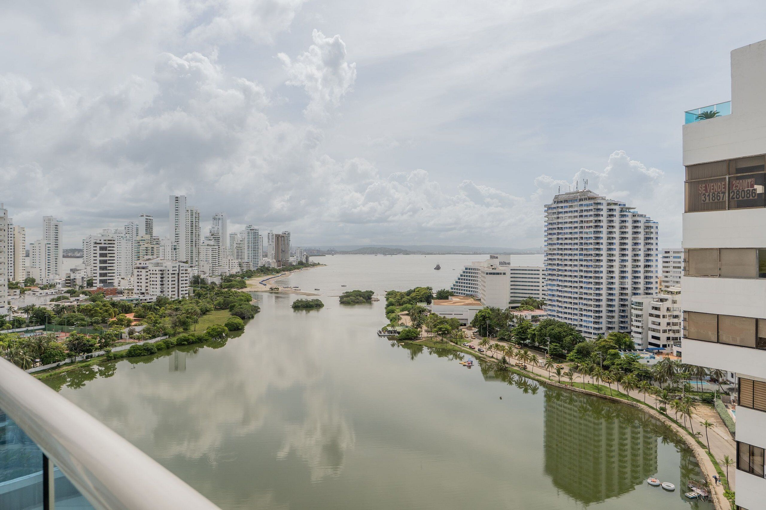 A high-rise hotel overlooking a calm river with a park and other buildings in the background.